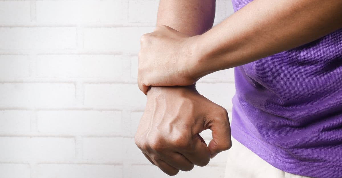 Close-up of a person's hands, one gripping the opposite wrist, against a white brick wall