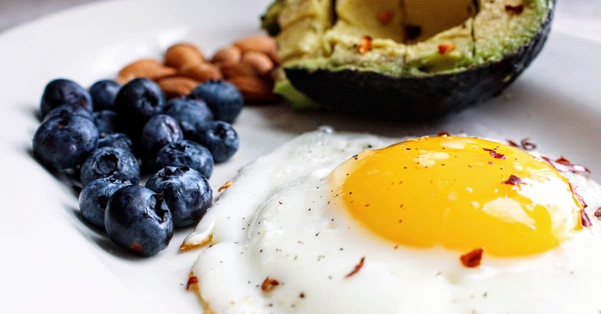 Close-up of a low-carbohydrate breakfast plate with a fried egg, half an avocado, almonds and fresh blueberries