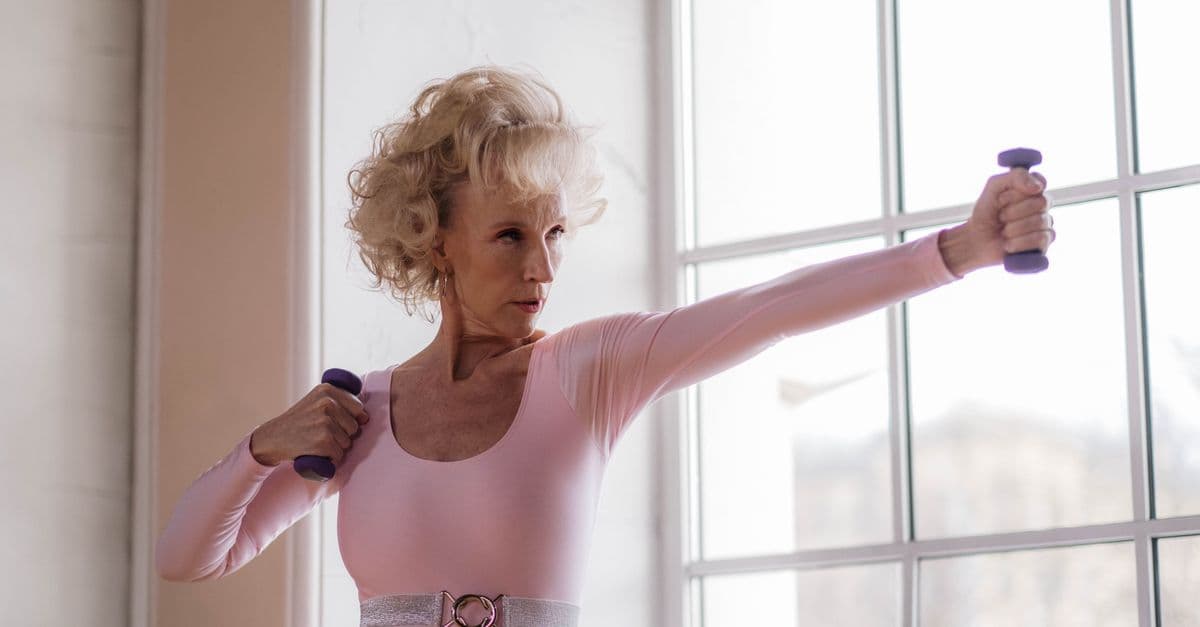 Older woman exercising with small hand weights beside a bright window