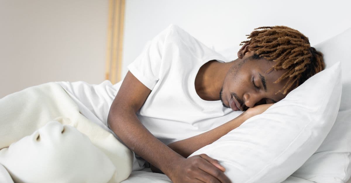 Man sleeping peacefully on his side on a white pillow under white bedding