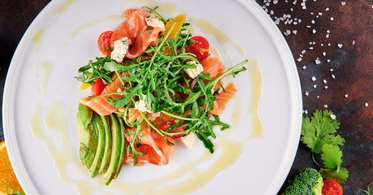 Overhead view of a plate of smoked salmon with sliced avocado, arugula, tomatoes and olive oil