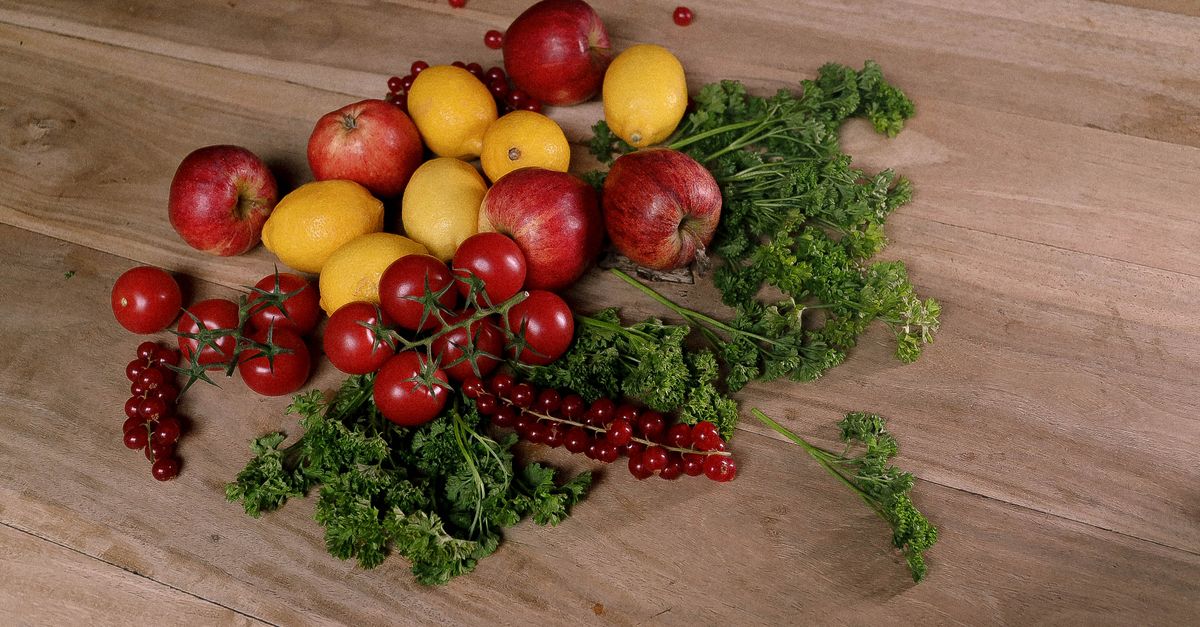 Fresh apples, lemons, vine tomatoes, red currants and curly parsley scattered on a rustic wooden table