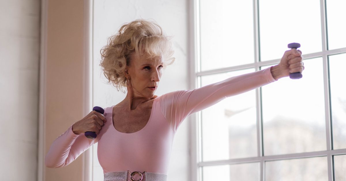 Older woman exercising with small hand weights beside a bright window